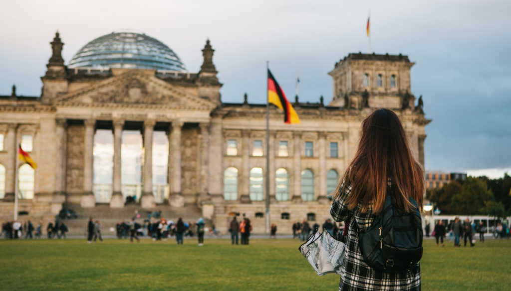 A tourist girl with a backpack next to the building called the Reichstag in Berlin in Germany takes pictures. Sightseeing, tourism, travel around Europe